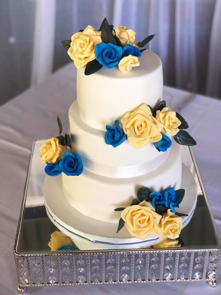 three tier white wedding cake with blue and yellow hand made sugar flowers